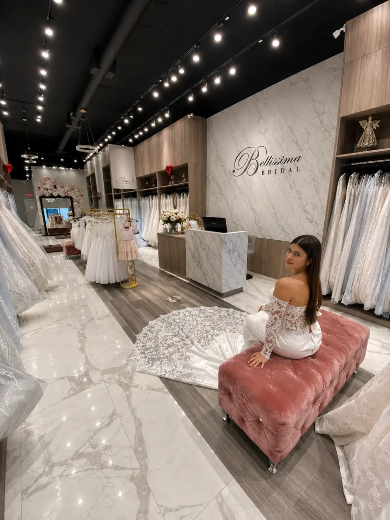 The Bellissima Bridal floor on Miracle Mile — gown rails, the marble wordmark wall and a bride on the velvet ottoman